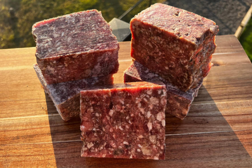 Blocks of Rabbit, Beef, Bison Mix on a wooden board, showcasing premium raw dog food ingredients.