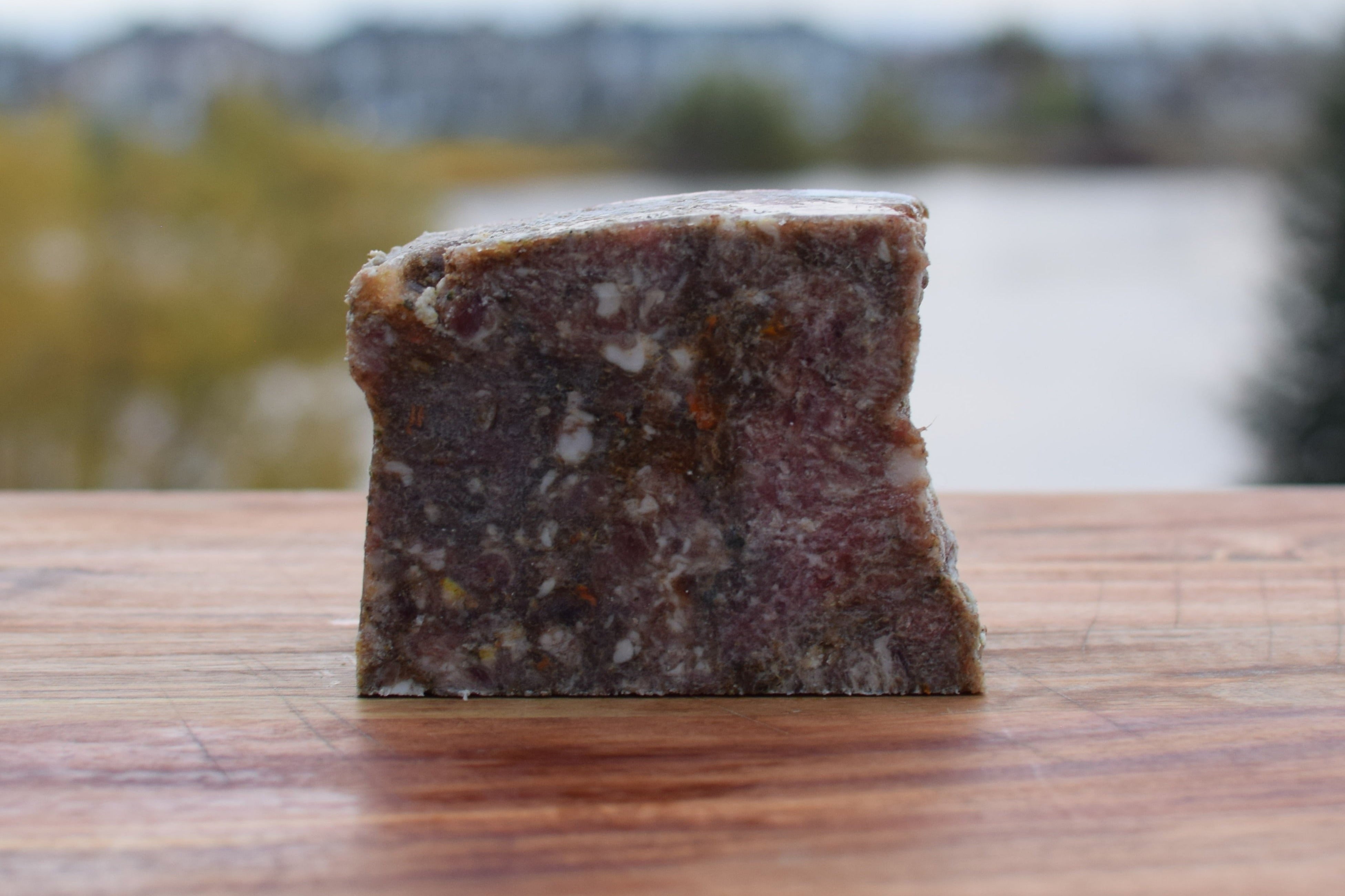Block of beef and bison vegetable mix on wooden surface with blurred background, perfect for raw pet food.