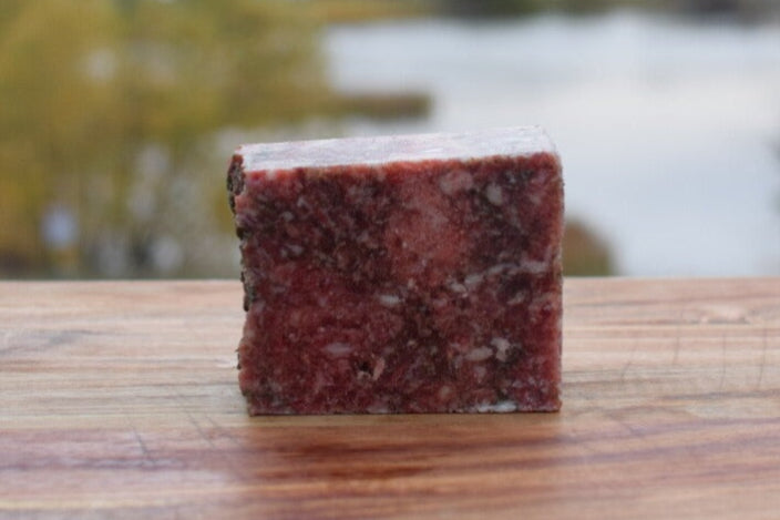 Raw chicken, beef, and bison mix for pets on a wooden surface with a blurred lake background.