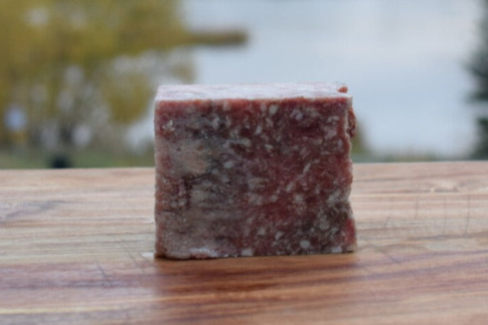 1 pound block of Duck, Beef, Bison mix dog food on a wooden surface with a scenic lake background.