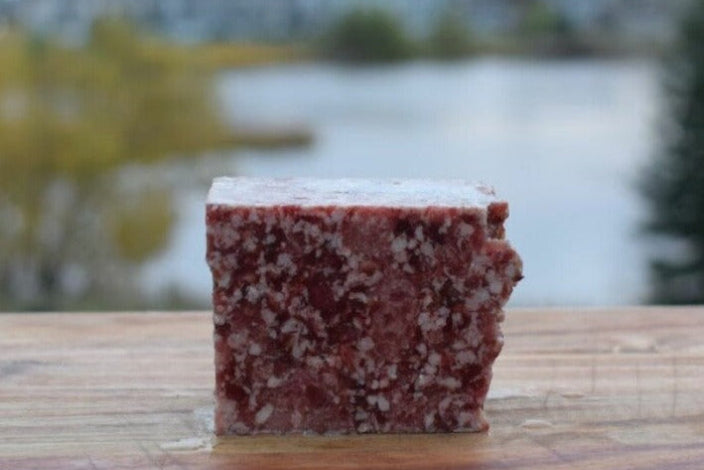 Turkey, beef, and bison raw dog food block on wooden surface with natural scenery in background.